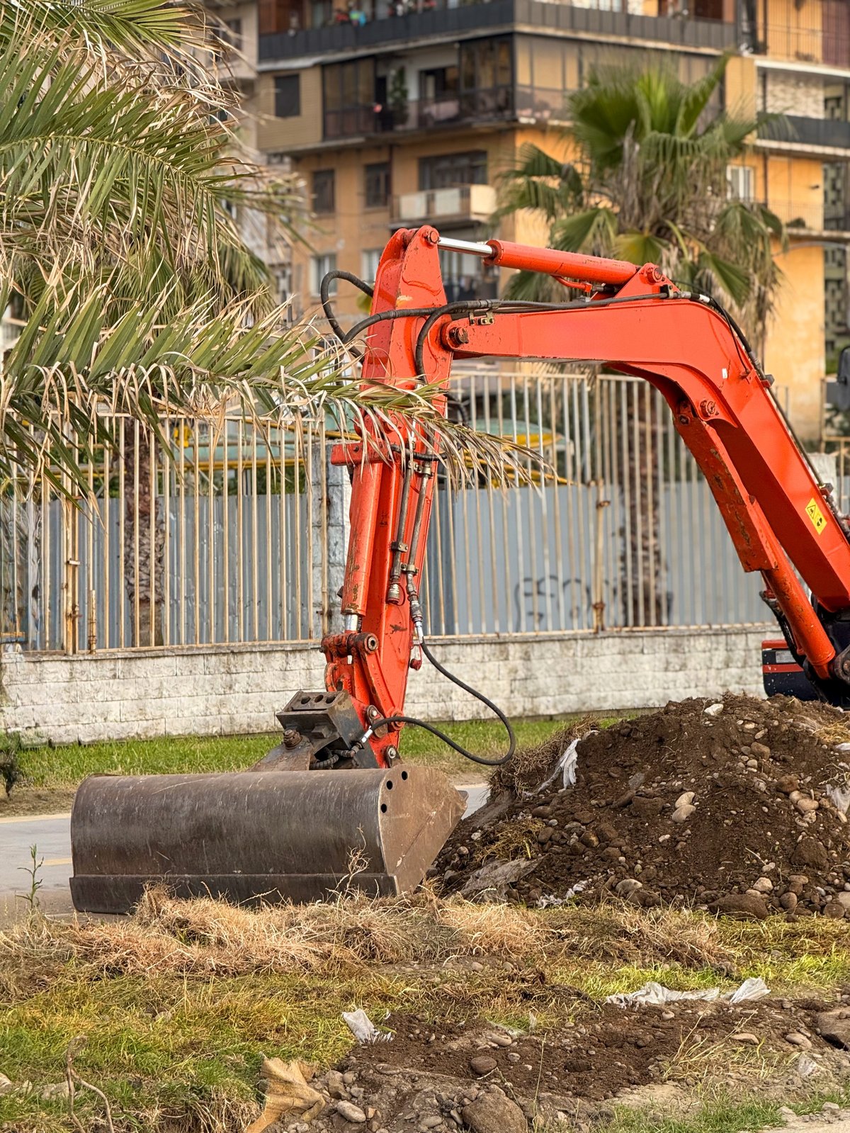 Excavator scooping dirt beside a fence on a cleared residential lot