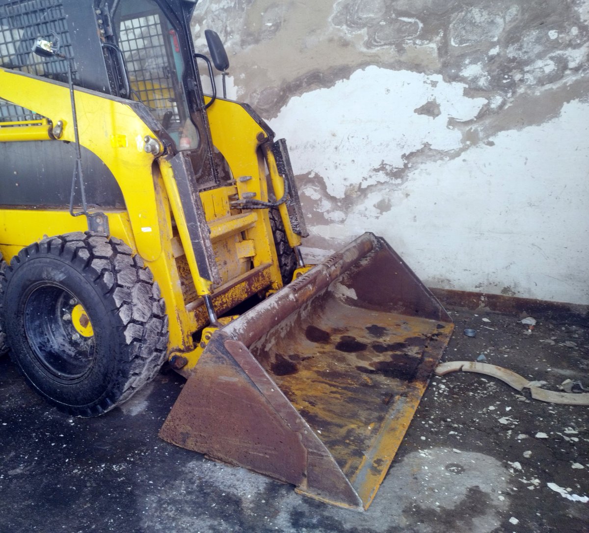 Close-up of a yellow skid-steer loader with its front bucket resting on the ground
